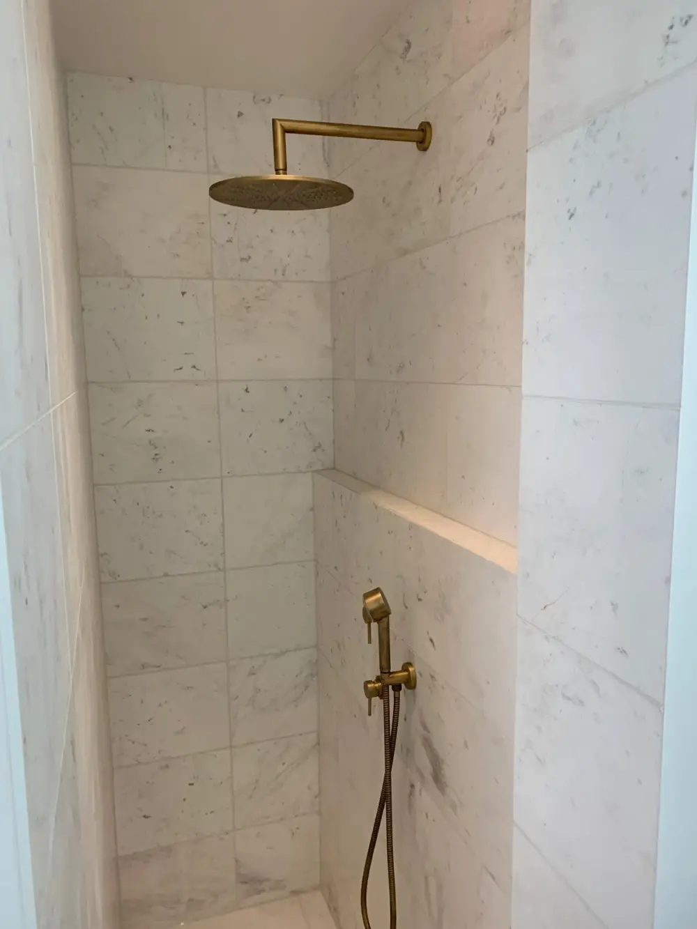 Douche rénovée avec carrelage effet marbre et robinetterie dorée en Île-de-France