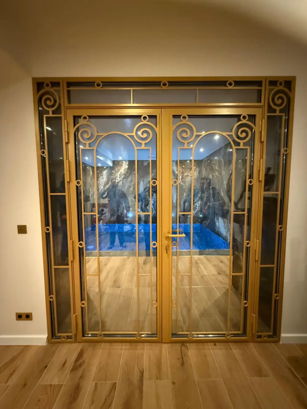 Espace piscine intérieure avec porte vitrée dorée et sol effet bois