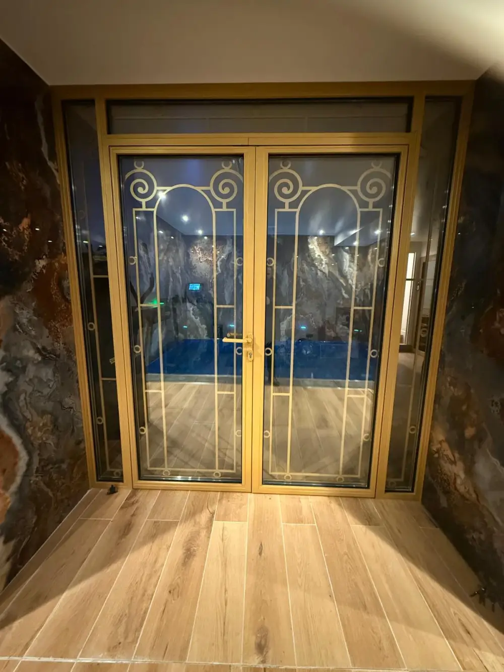 Accès vitré à une piscine intérieure avec menuiseries dorées