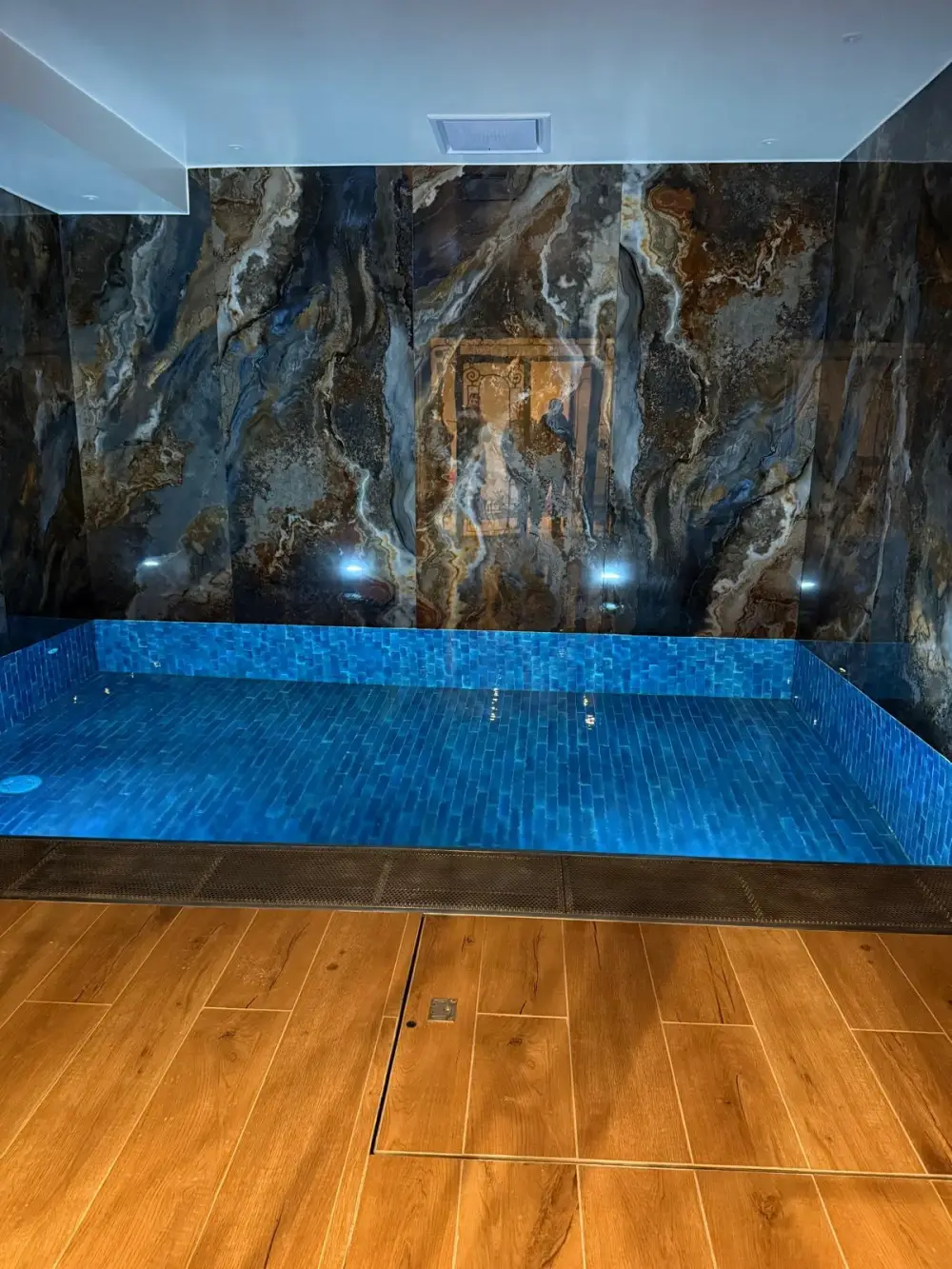 Piscine intérieure rénovée avec mosaïque bleue et murs effet marbre
